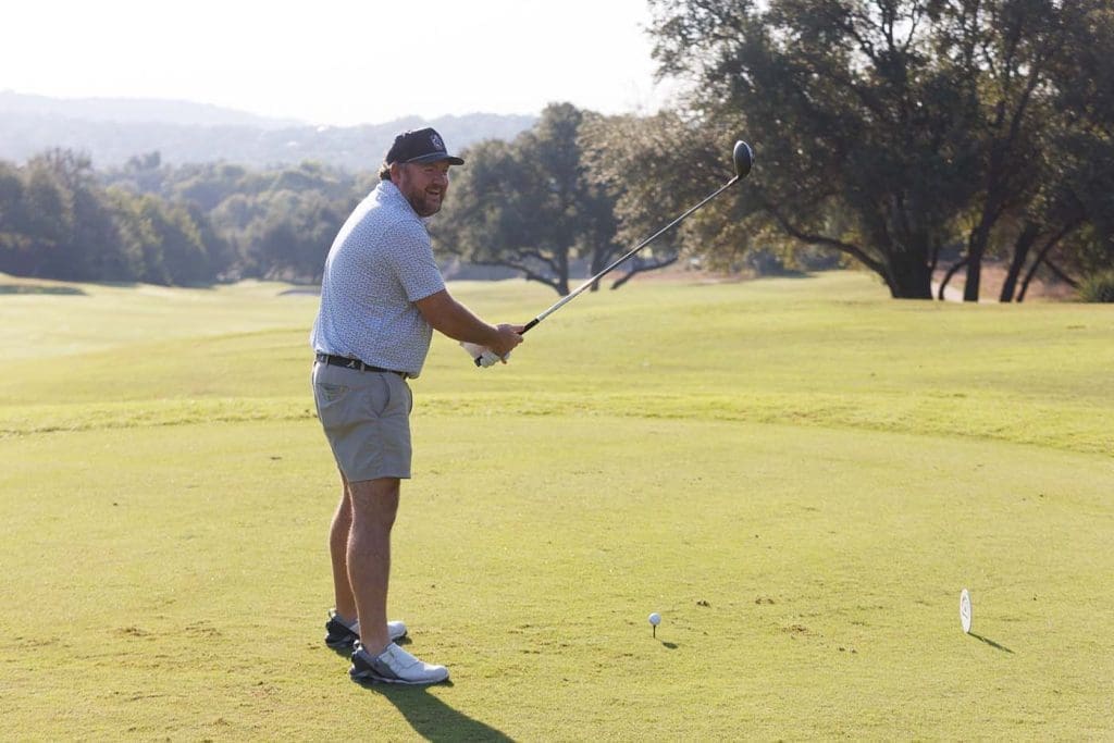 A man stands on a golf course holding a golf club, preparing to hit a ball that is positioned on a tee.