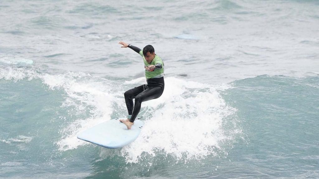 A person in a green shirt and black wetsuit is riding a wave on a surfboard in the ocean.